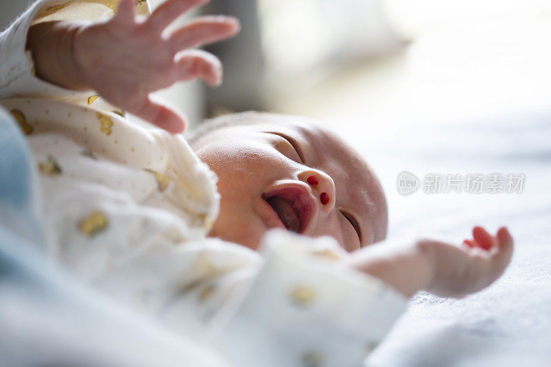 Cute newborn baby lying on bed, crying. Close up.